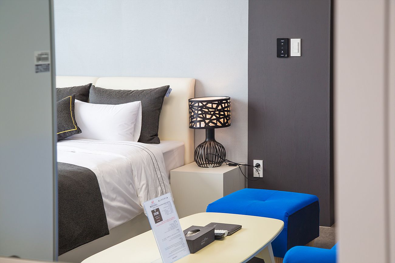 Ein Hotelzimmer mit einem Bett, einem Nachttisch mit Lampe, einem kleinen blauen Stuhl und einem Schild auf dem Tisch.