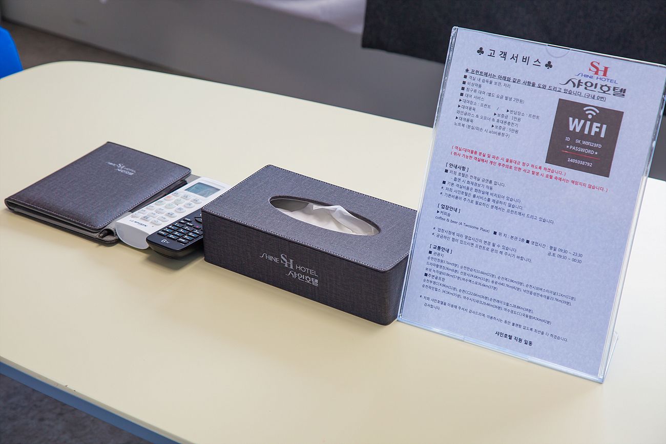 Un comptoir d’accueil d’hôtel avec un panneau indiquant la disponibilité du Wi-Fi, une boîte de mouchoirs et un téléphone portable.
