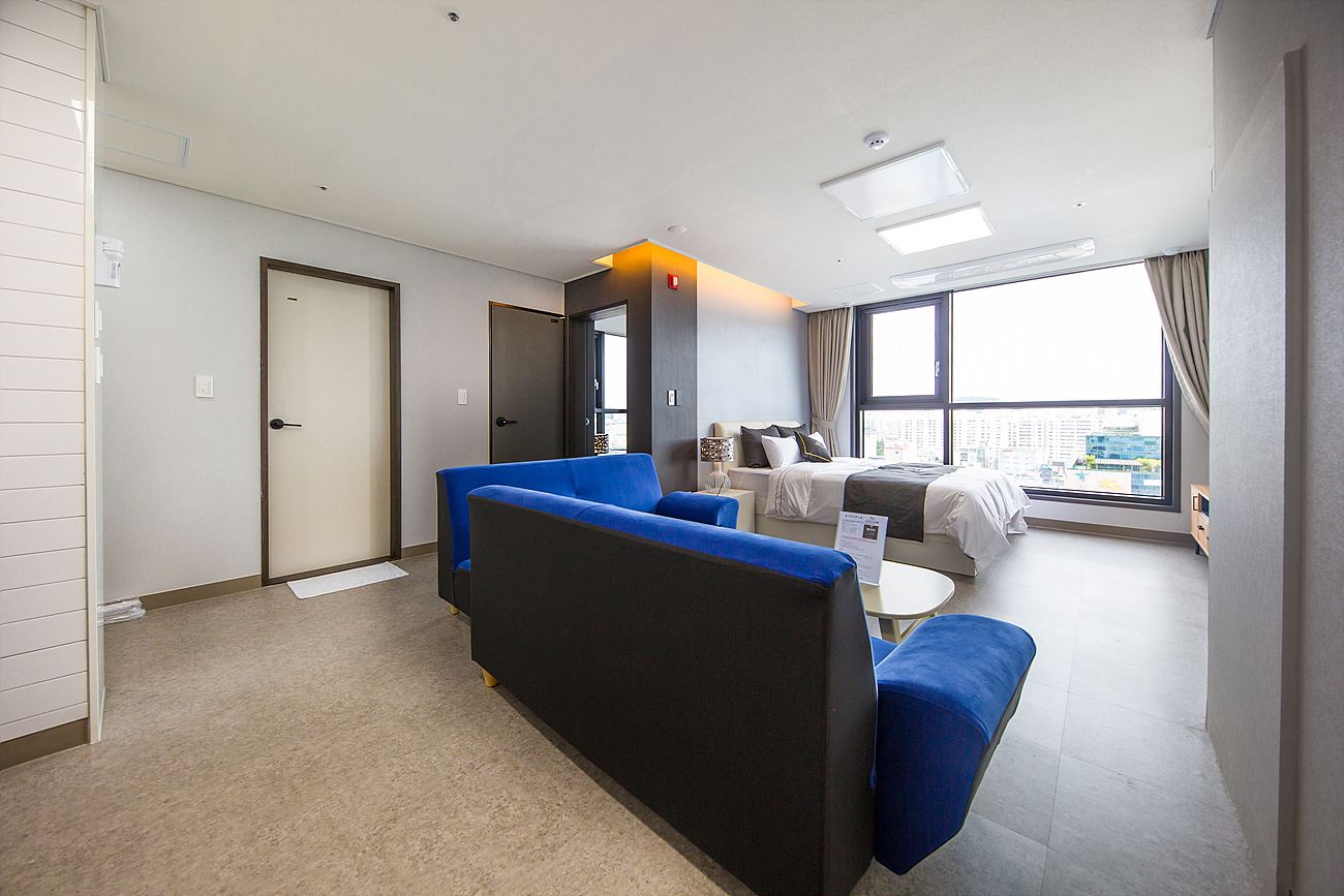 A modern hotel room with a sofa, a bed, a small table, and a large window offering a city view.