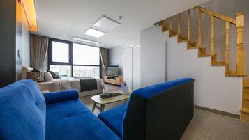 Ett modernt hotellrum med en stor säng, en blå soffa, ett litet bord och en trätrappa.