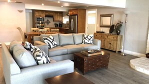 A modern living room with a sectional sofa, a wooden coffee table, and a kitchen in the background.