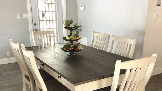 A dining area with a wooden table and six chairs, a decorative fruit centerpiece, and a door with a window.