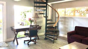 A modern interior with a spiral staircase, a desk with a lamp, a chair, and a sofa.