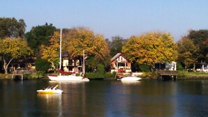 A lakeside view with boats, a house, and trees.