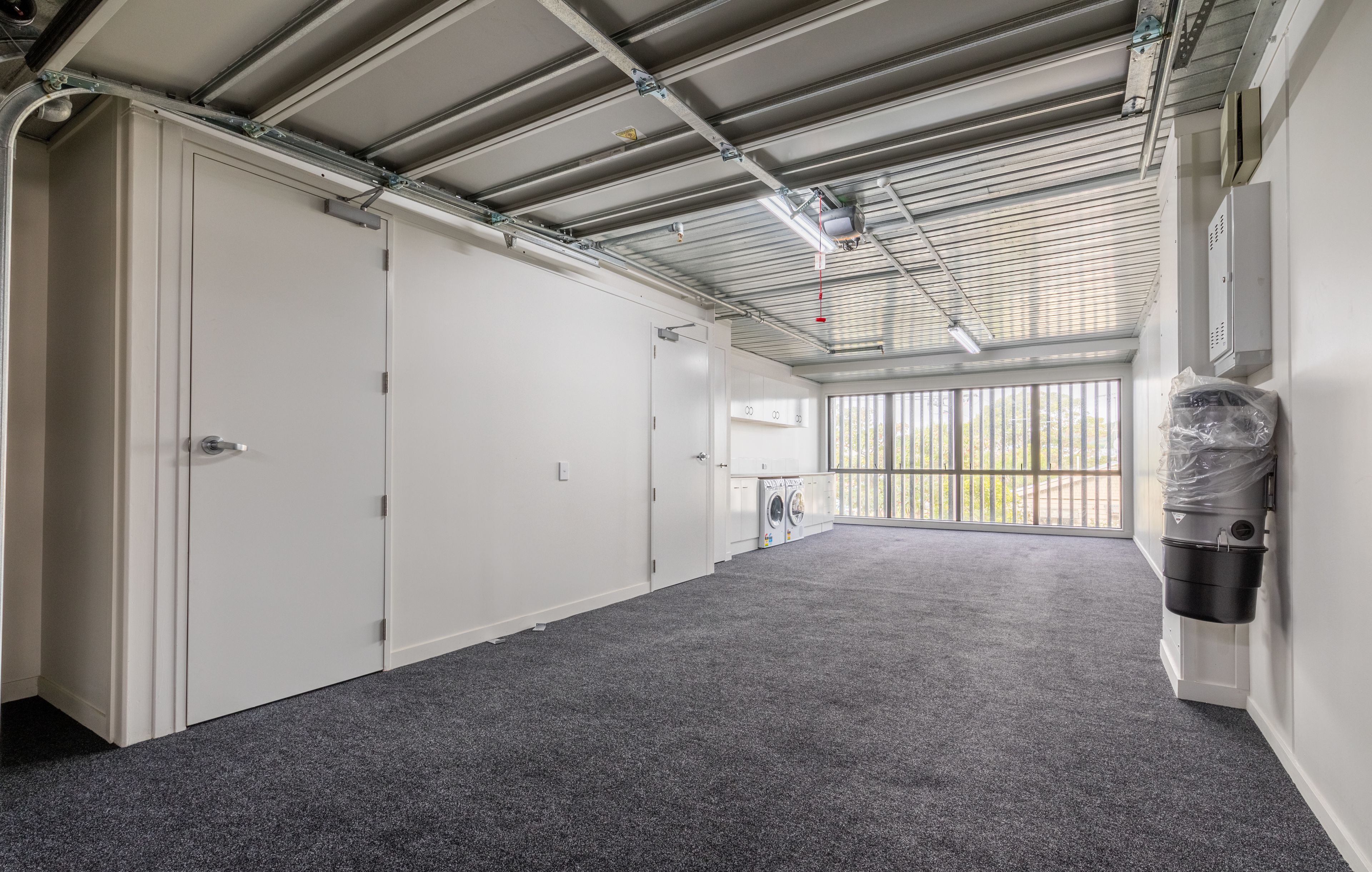 A clean, industrial-style room with a grey carpet, metal ceiling, and a large window with a view of greenery.