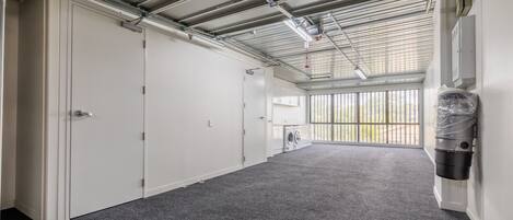 A clean, industrial-style room with a grey carpet, metal ceiling, and a large window with a view of greenery.