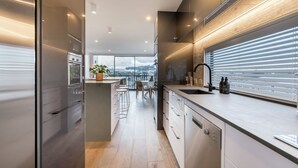 A modern kitchen with a large island, stainless steel appliances, and a view of the city through large windows. - Spacious 3 Bedroom with Ensuite Bathroom (Auckland)