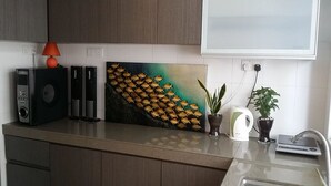 A kitchen with a countertop, a painting, a speaker, a kettle, and a potted plant.