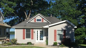 A two-story house with a front porch, a small garden, and a view of a lake. - Cozy Lakefront Home - 278 FIVE STAR Reviews - Kayaks, Sunsets & Panoramic Views (Newburgh)