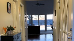 A hallway with wooden flooring, a patterned rug, a ceiling fan, and a view of a lake through large windows. - Cozy Lakefront Home - 278 FIVE STAR Reviews - Kayaks, Sunsets & Panoramic Views (Newburgh)