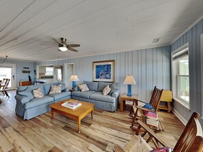 A living room with a blue-striped couch, a wooden coffee table, and a ceiling fan.