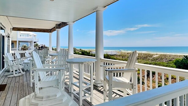 A covered outdoor deck with white Adirondack chairs and a table, overlooking a beach. - Oceans 111 | Oceanfront with Elevator + Direct Beach Access! (Topsail Beach)