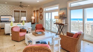 A spacious living room with wicker furniture, a white coffee table, and a television. Large windows offer a view of the ocean. - Oceans 111 | Oceanfront with Elevator + Direct Beach Access! (Topsail Beach)
