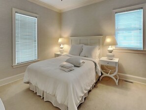 A bedroom with a large bed, two bedside tables with lamps, and windows with blinds. - Oceans 111 | Oceanfront with Elevator + Direct Beach Access! (Topsail Beach)
