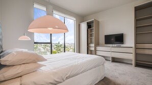 Ein Schlafzimmer mit einem großen Bett, einem Fernseher, einem Kleiderschrank und einem Fenster mit Blick auf die Stadt.