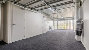 Ein aufgeräumter, im Industriedesign gestalteter Raum mit grauem Teppich, Metalldecke und einem großen Fenster mit Blick ins Grüne.