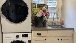 A laundry area with two Samsung front-loading washers, a sink with a faucet, and a window with blinds.