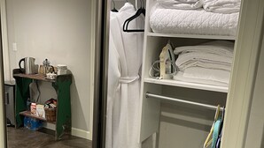 A bedroom with a large mirror, a closet with neatly folded bedding, and a shelf with toiletries.