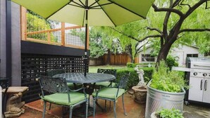 An outdoor patio with a round table and chairs, a green umbrella, and potted plants.