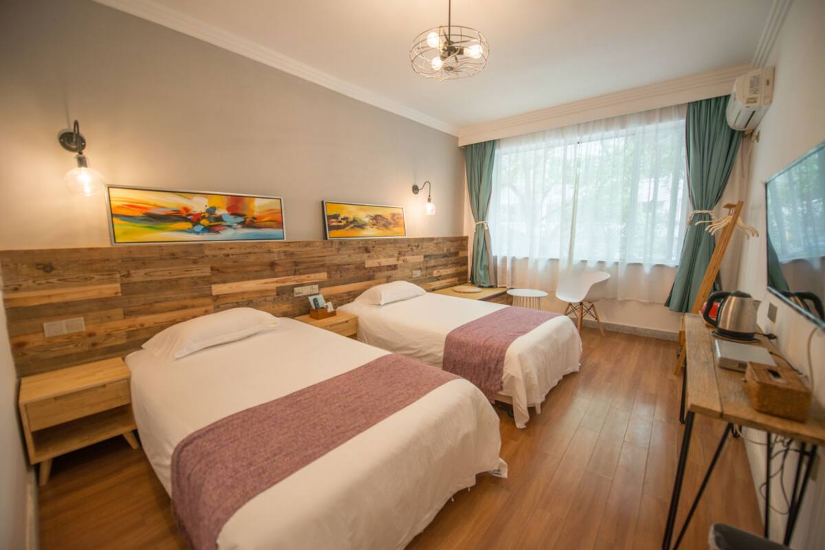 A hotel room with two beds, a wooden headboard, a desk with a chair, a television, and artwork on the wall.