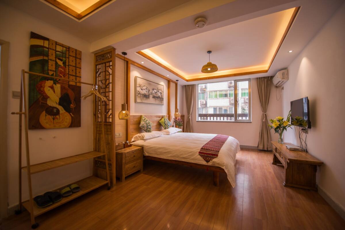 A bedroom with a wooden bed, a nightstand, a TV, and a window with curtains.