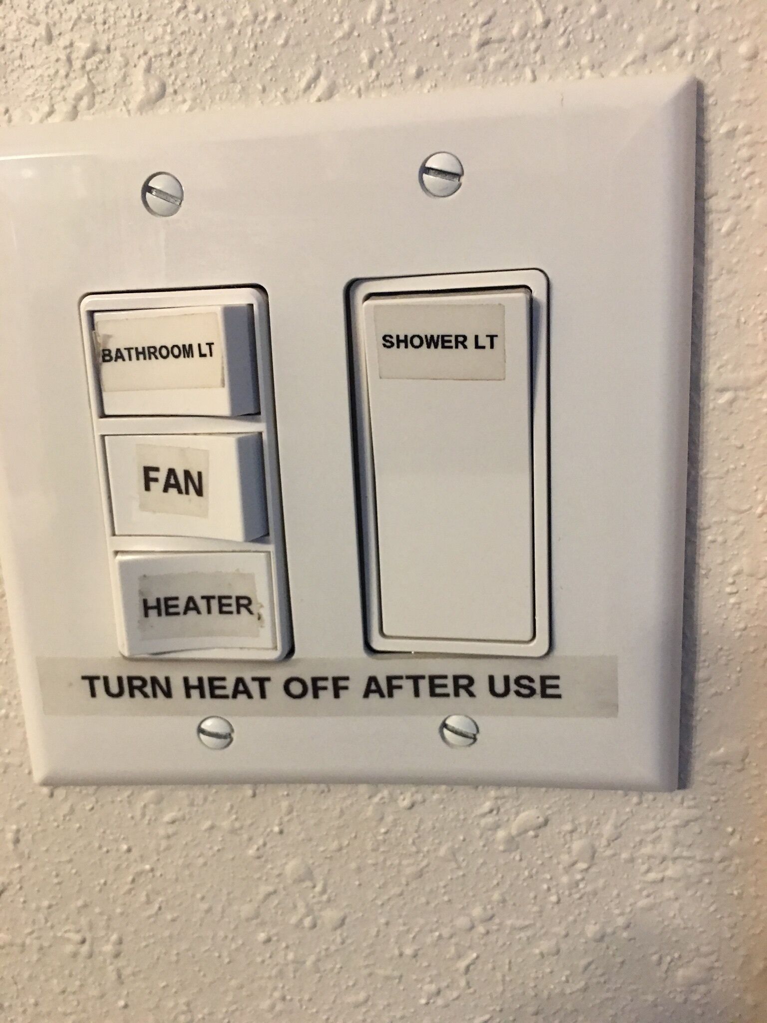 Ein an der Wand montiertes Bedienfeld mit Tasten für 'BADEZIMMER LINKS', 'SHOWER LINKS', 'VENTILATOR', 'HEIZER' und der Aufforderung 'HEIZUNG NACH BENUTZUNG AUSSCHALTEN'.