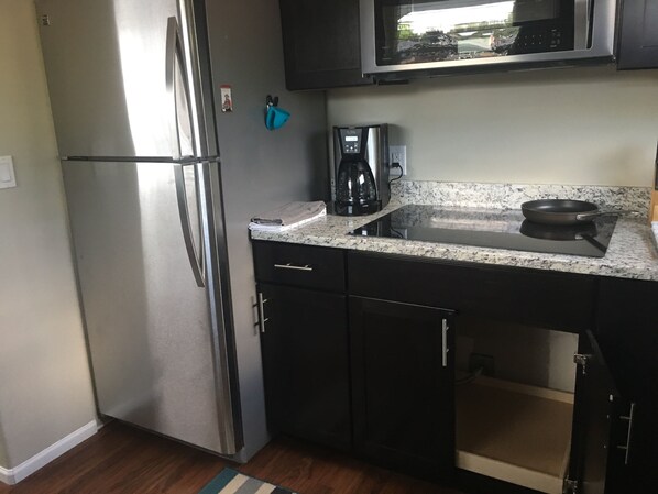 A compact kitchen with a stainless steel refrigerator, a microwave, a coffee maker, and a stovetop. - Pacific Northwest Studio Cottage (Puyallup)