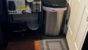 A compact kitchenette with a Bella air fryer, a toaster, and a stainless steel trash can.
