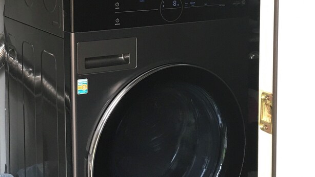 A black stacked washer and dryer unit with a control panel and a small sticker on the door.