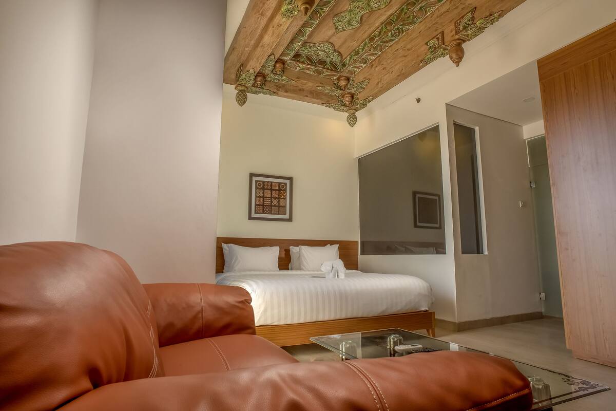 Une chambre d’hôtel moderne avec un canapé en cuir, un lit en bois, une table basse en verre et un grand miroir.