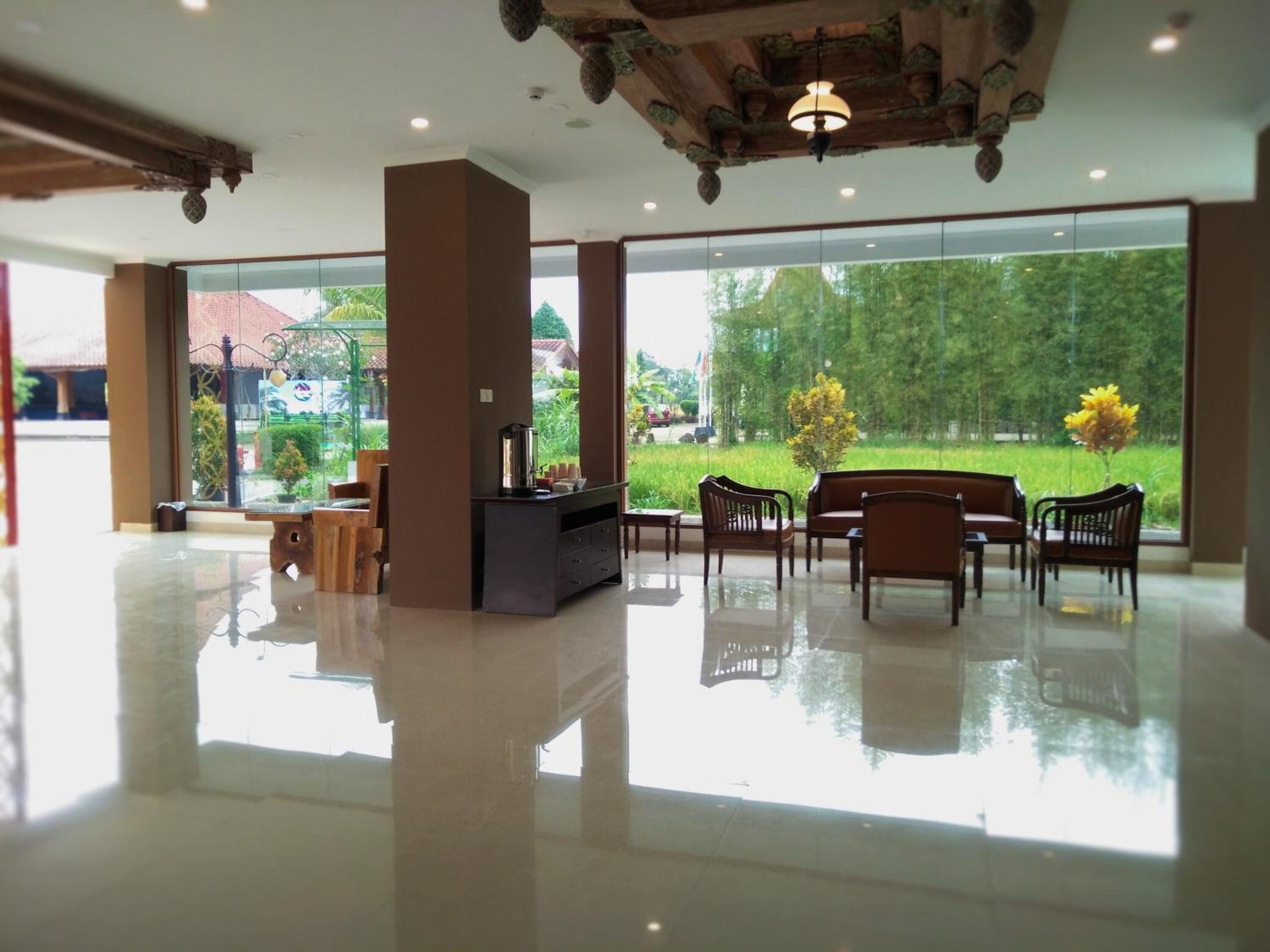 A spacious lobby with a reception desk, seating area, and large windows offering a view of greenery and buildings.