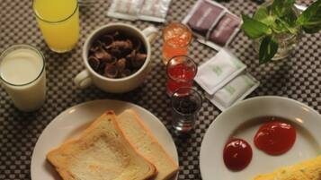 A table with a checkered tablecloth, a glass of orange juice, a cup of hot chocolate, a plate with toast, a plate with ketchup, and a small plant.