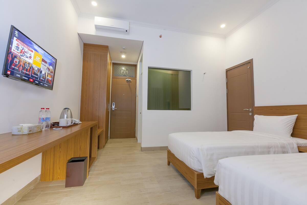 Une chambre d’hôtel avec un bureau en bois, deux lits, une télévision et une fenêtre.