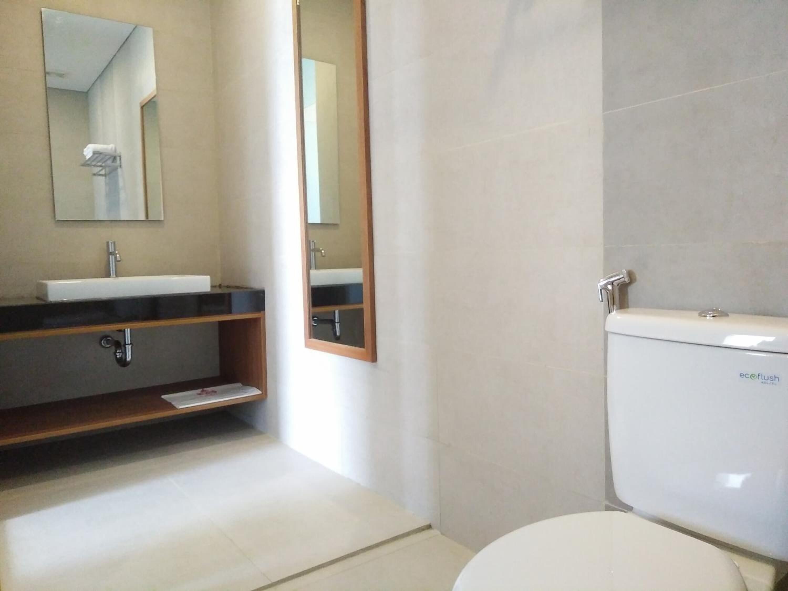 Un baño moderno con un inodoro blanco, un lavabo con espejo arriba y un estante debajo.