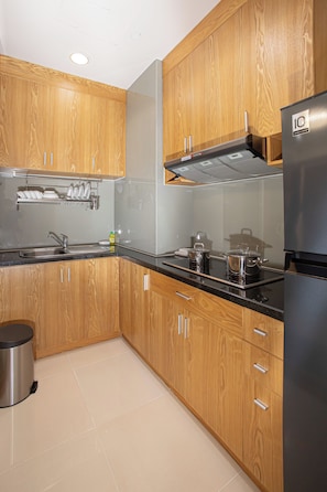 A modern kitchen with wooden cabinets, a stainless steel sink, and a black countertop. - Mayfair Suites (Ho Chi Minh City)