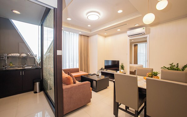 A modern hotel room with a kitchenette, a sofa, a dining area, and a television. - Mayfair Suites (Ho Chi Minh City)