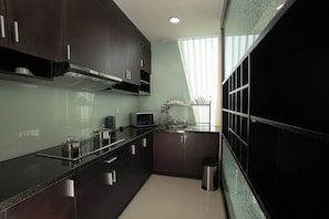 A modern kitchen with dark cabinets, stainless steel appliances, and a window with sheer curtains. - Mayfair Suites (Ho Chi Minh City)
