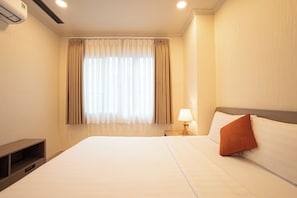 Quarto de hotel com uma cama grande, abajur e janela com cortinas.