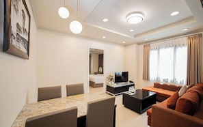 A hotel room with a dining area, a living area with a sofa and TV, a bed, and a bathroom visible through an open door. - Mayfair Suites (Ho Chi Minh City)