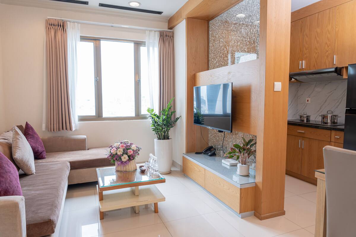 A modern living room with a sofa, coffee table, TV, and kitchen area.