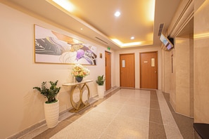 A hotel lobby with a reception desk, a large abstract painting, two potted plants, and a tiled floor. - Mayfair Suites (Ho Chi Minh City)