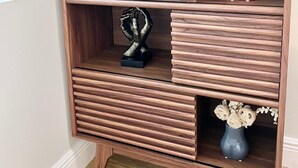 A wooden sideboard with multiple shelves, a framed picture, and two vases with dried flowers. - Miami Beach HomeStay (North Miami)