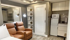 A compact bedroom with a brown leather chair, a bed, a white wardrobe, a microwave, and a small kitchenette. - Miami Beach HomeStay (North Miami)