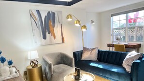 A modern living room with a grey armchair, a blue sofa, and a round coffee table. There is a painting on the wall and a desk with a chair in the background. - Miami Beach HomeStay (North Miami)