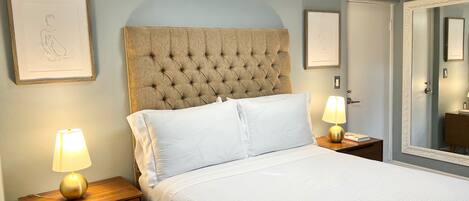 A neatly made bed with white linens, a tufted headboard, and two bedside lamps on wooden nightstands.