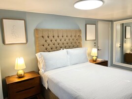 Una cama bien hecha con ropa blanca, un cabecero capitonado y dos lámparas de noche sobre mesitas de madera.