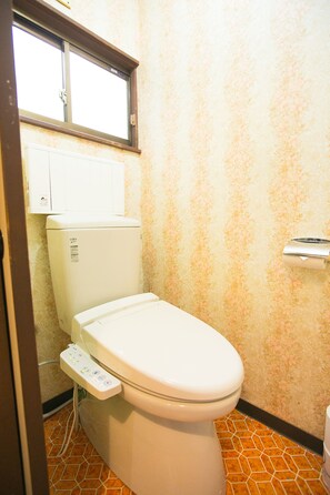 Des toilettes classiques dotées d’un panneau de commande, d’une fenêtre située au-dessus et d’un mur orné d’un motif.