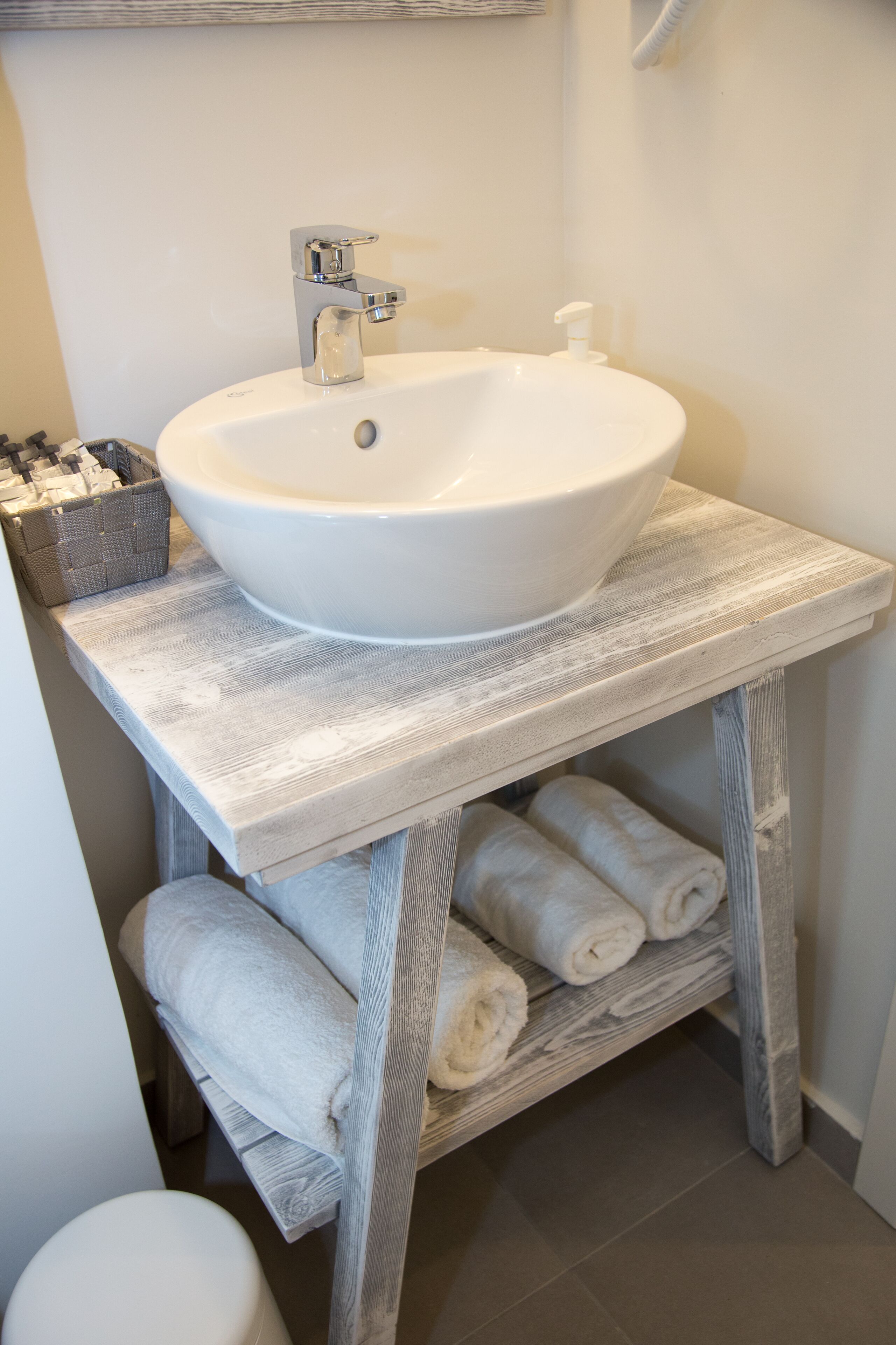 Un baño con un lavabo blanco sobre un mueble de madera rústica, un inodoro y toallas dobladas con cuidado.