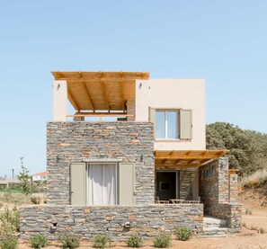 Una casa moderna de dos pisos con fachada de piedra, una pérgola de madera en el nivel superior y un balcón pequeño.