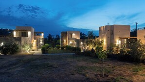 A modern villa with multiple levels, stone walls, and a well-lit garden area. - Vourkari Village (Kea)